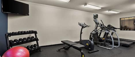 Un gimnasio con equipo de ejercicio, un televisor y una estantería de pared con mancuernas.