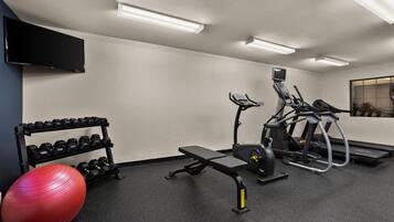 A gym with exercise equipment, a TV, and a wall-mounted shelf with dumbbells.