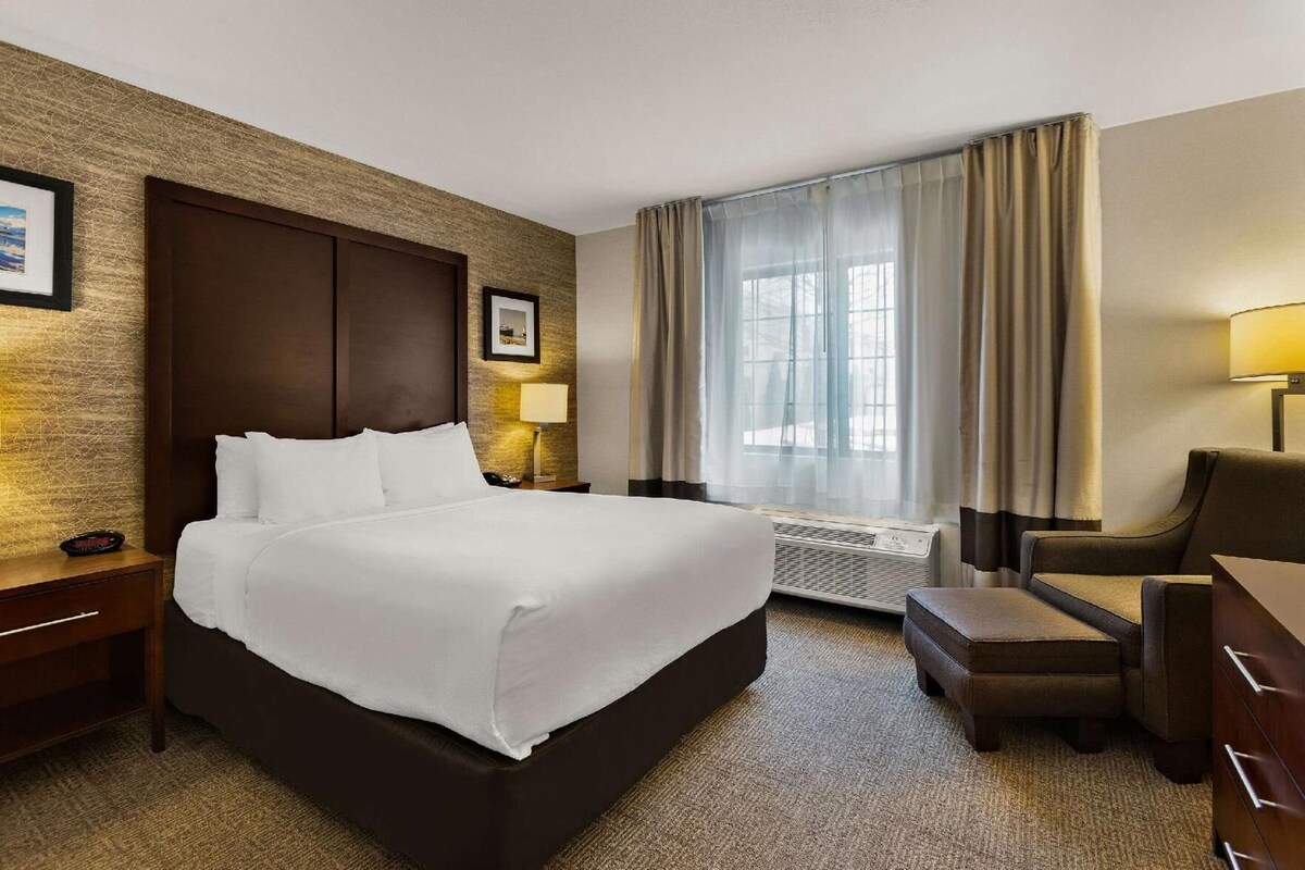 A hotel room with a large bed, a chair, a desk, a lamp, and a window with curtains.