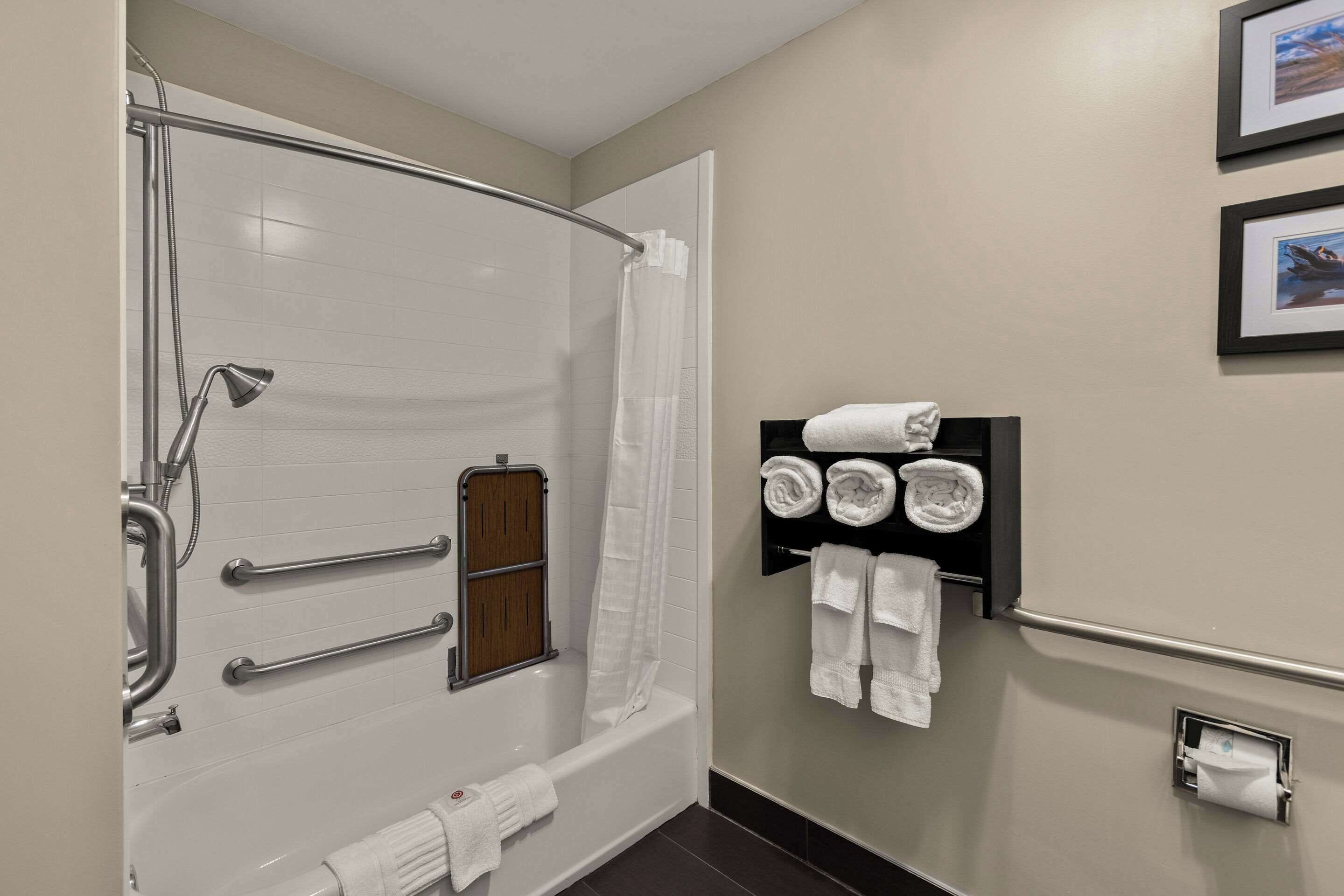 Un baño moderno con ducha a ras de suelo, barras de apoyo, toallero y dispensador de papel higiénico.