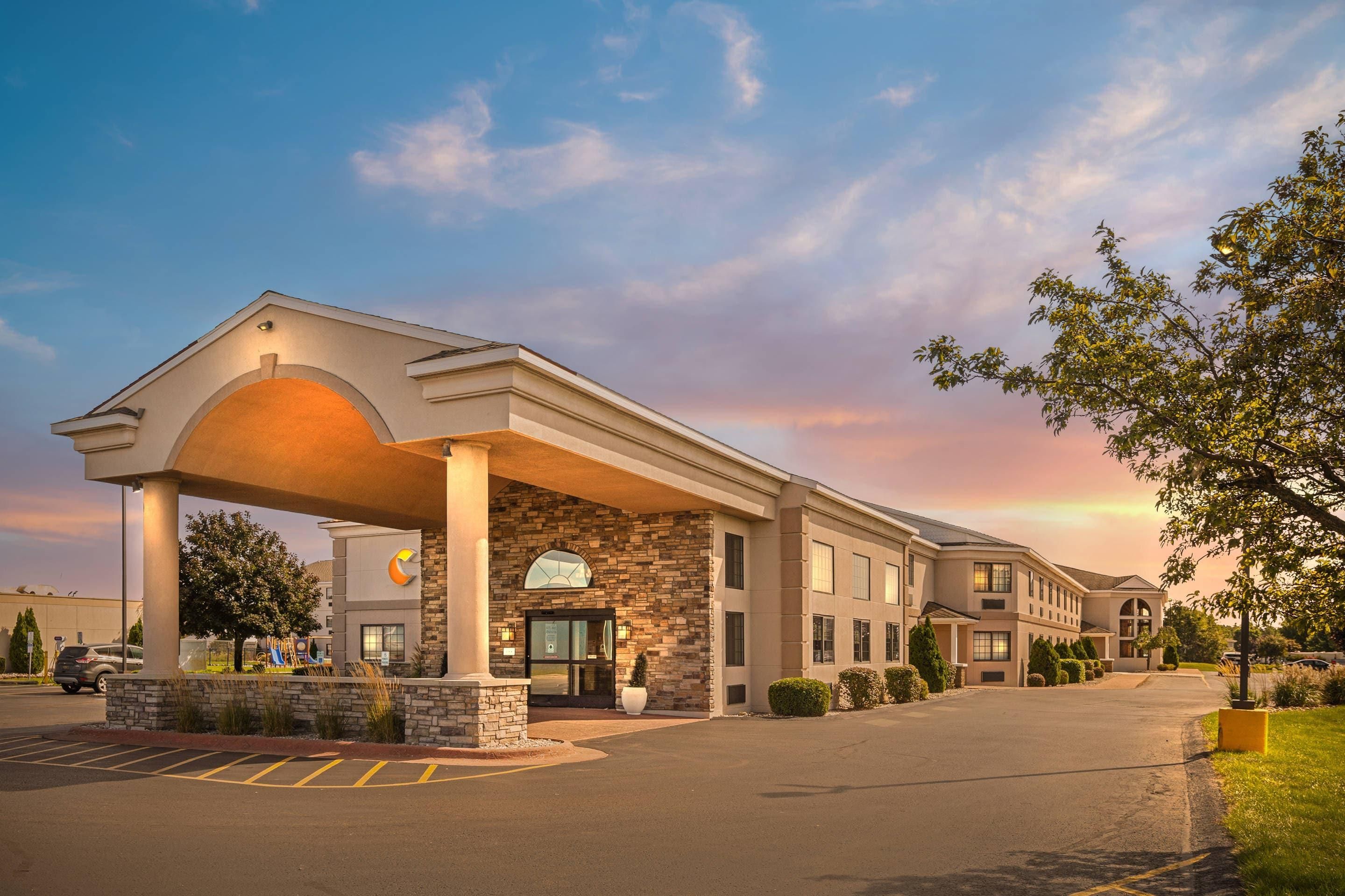 A hotel with a covered entrance, a parking lot, and a landscaped area with trees.