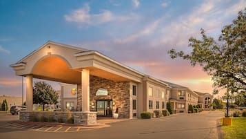 A hotel with a covered entrance, a parking lot, and a landscaped area with trees.