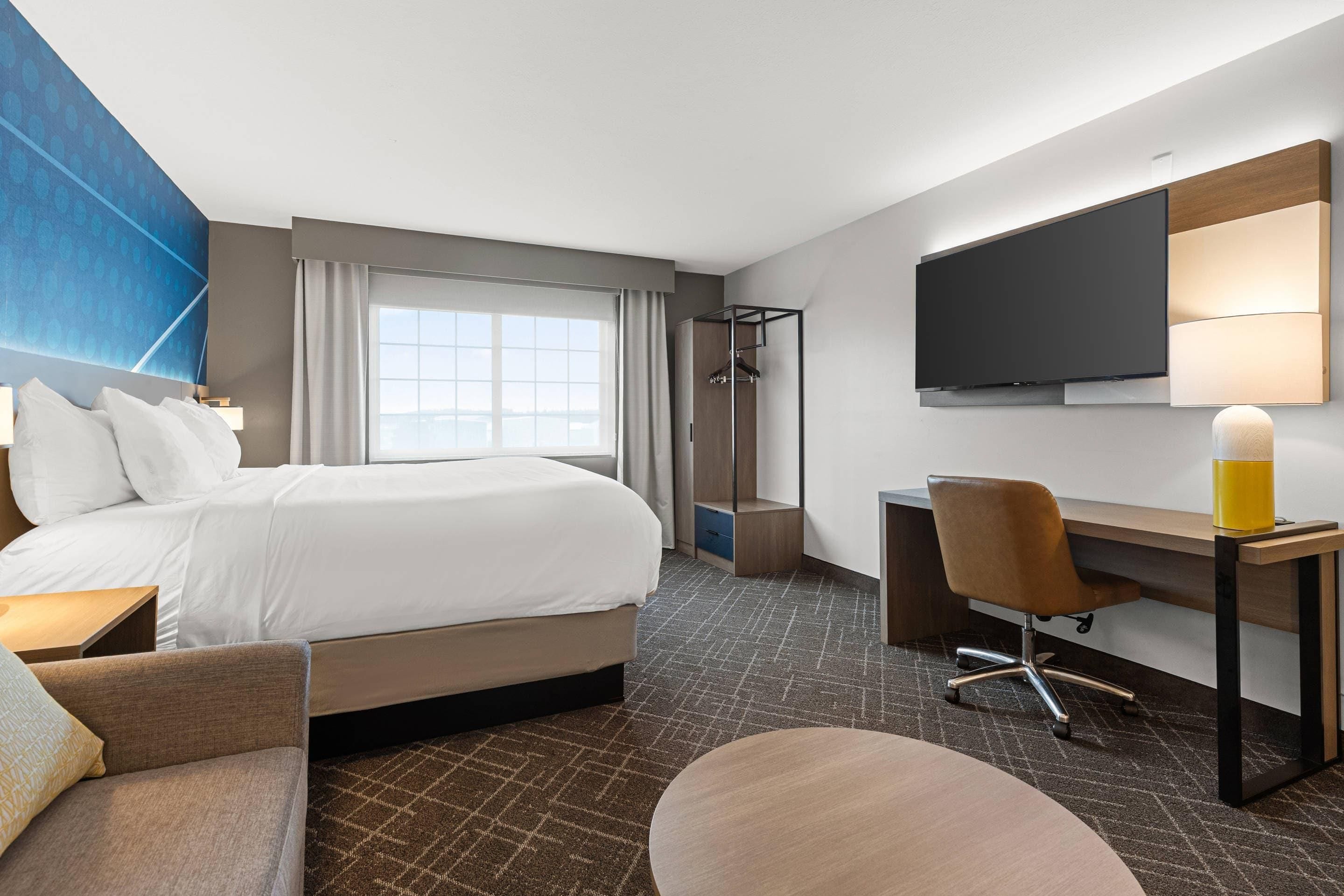Habitación de hotel con cama, escritorio, silla, televisión y ventana con cortinas.