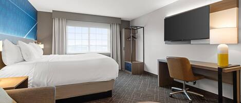 Habitación de hotel con cama, escritorio, silla, televisión y ventana con cortinas.