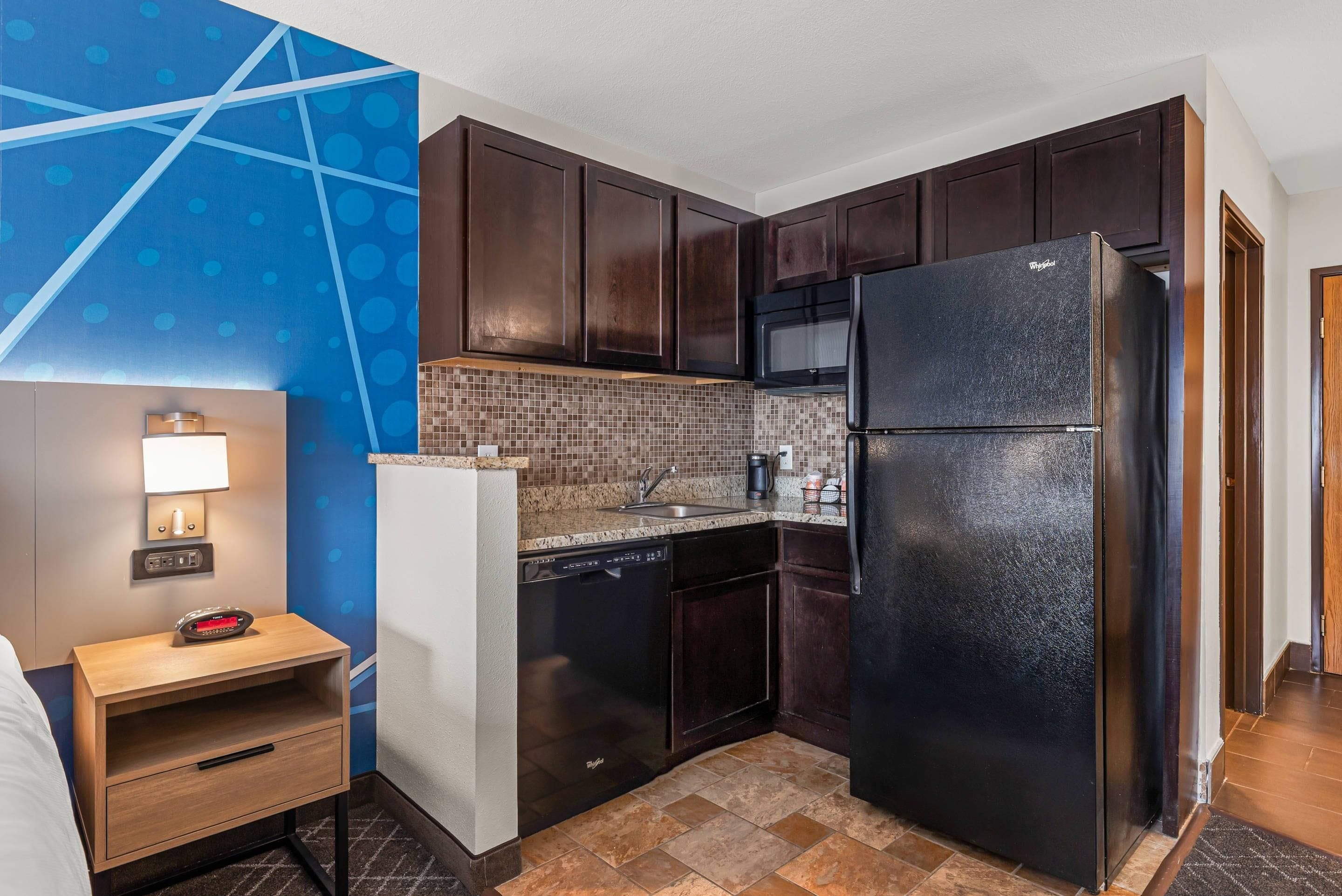 Una cocina compacta con muebles oscuros de madera, un refrigerador negro, un microondas y un salpicadero de azulejos.