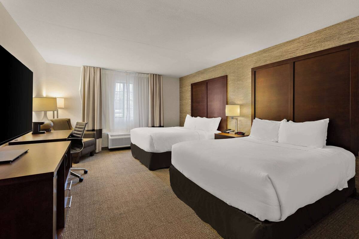 A hotel room with two beds, a desk, a TV, and a window with curtains.