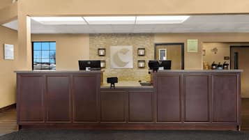 A reception area with a wooden reception desk, two computer monitors, a large abstract wall art piece, and framed pictures on the wall.