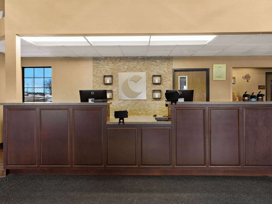 A reception area with a wooden reception desk, two computer monitors, a large abstract wall art piece, and framed pictures on the wall.