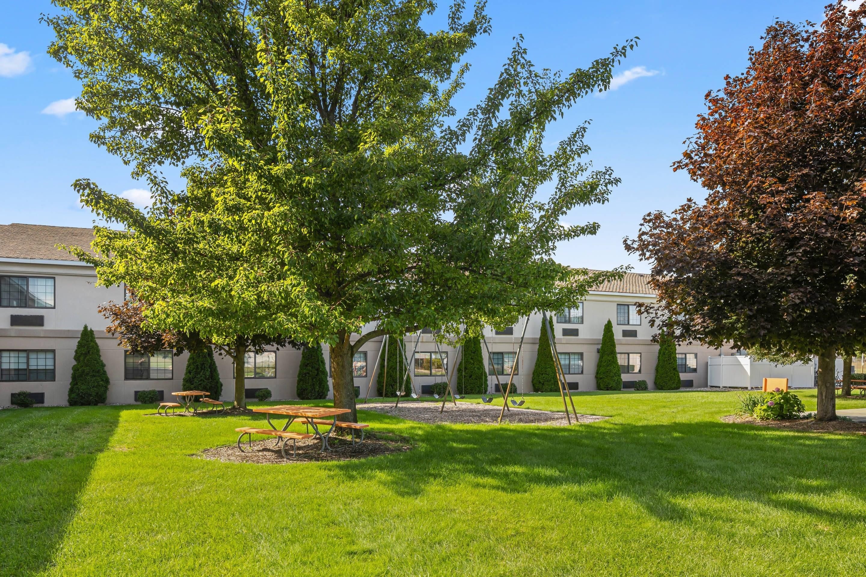 A courtyard with a lawn, picnic tables, and swings.