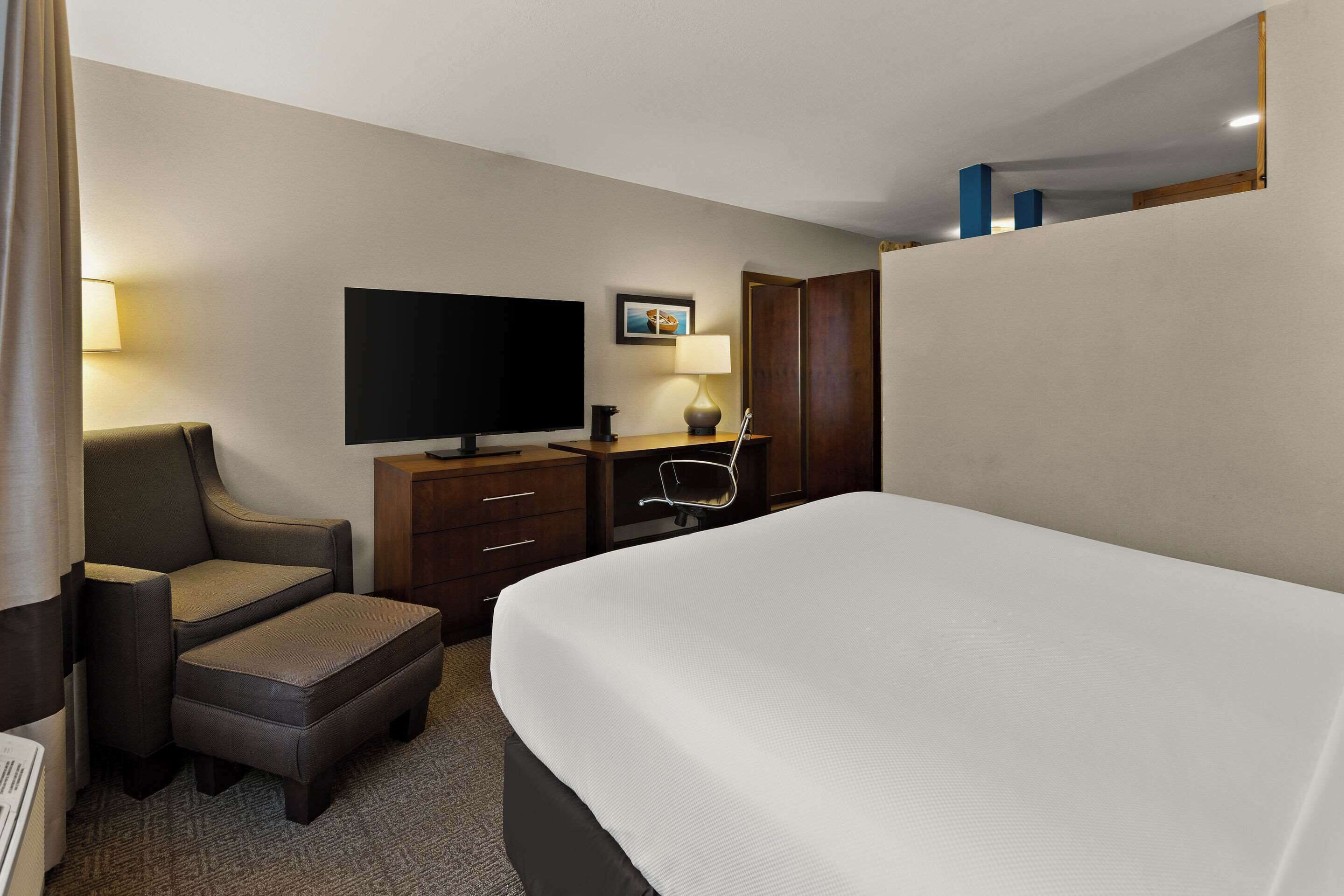 A hotel room with a large bed, a television, a desk with a chair, and a wardrobe.