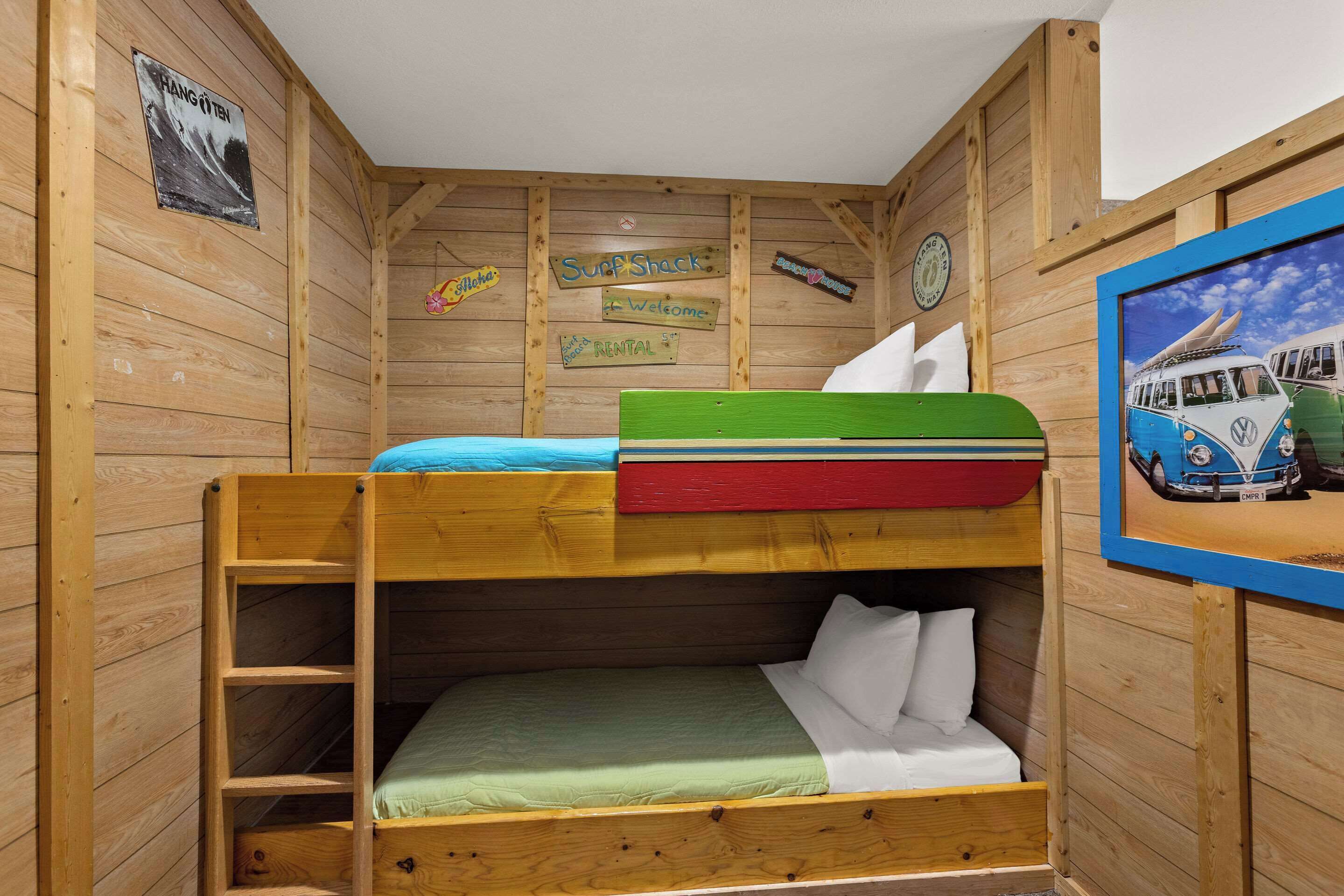 A bunk bed room with wooden walls, a ladder, and various signs including 'Surf Shack' and 'Welcome'.
