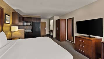 A hotel room with a bed, a TV on a wooden dresser, a kitchen area, and a bathroom.