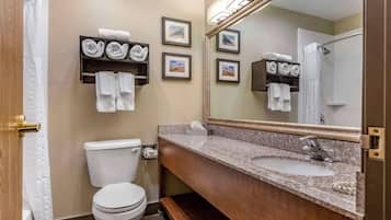 A bathroom with a toilet, sink, and mirror. There are towels and framed pictures on the wall.