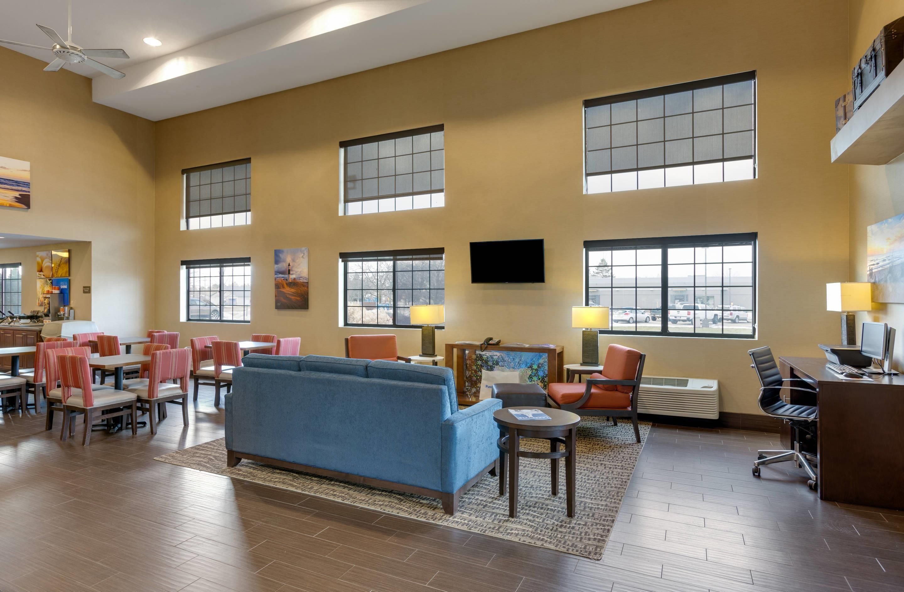 A spacious hotel lobby with multiple seating areas, large windows, and a flat-screen TV mounted on the wall.
