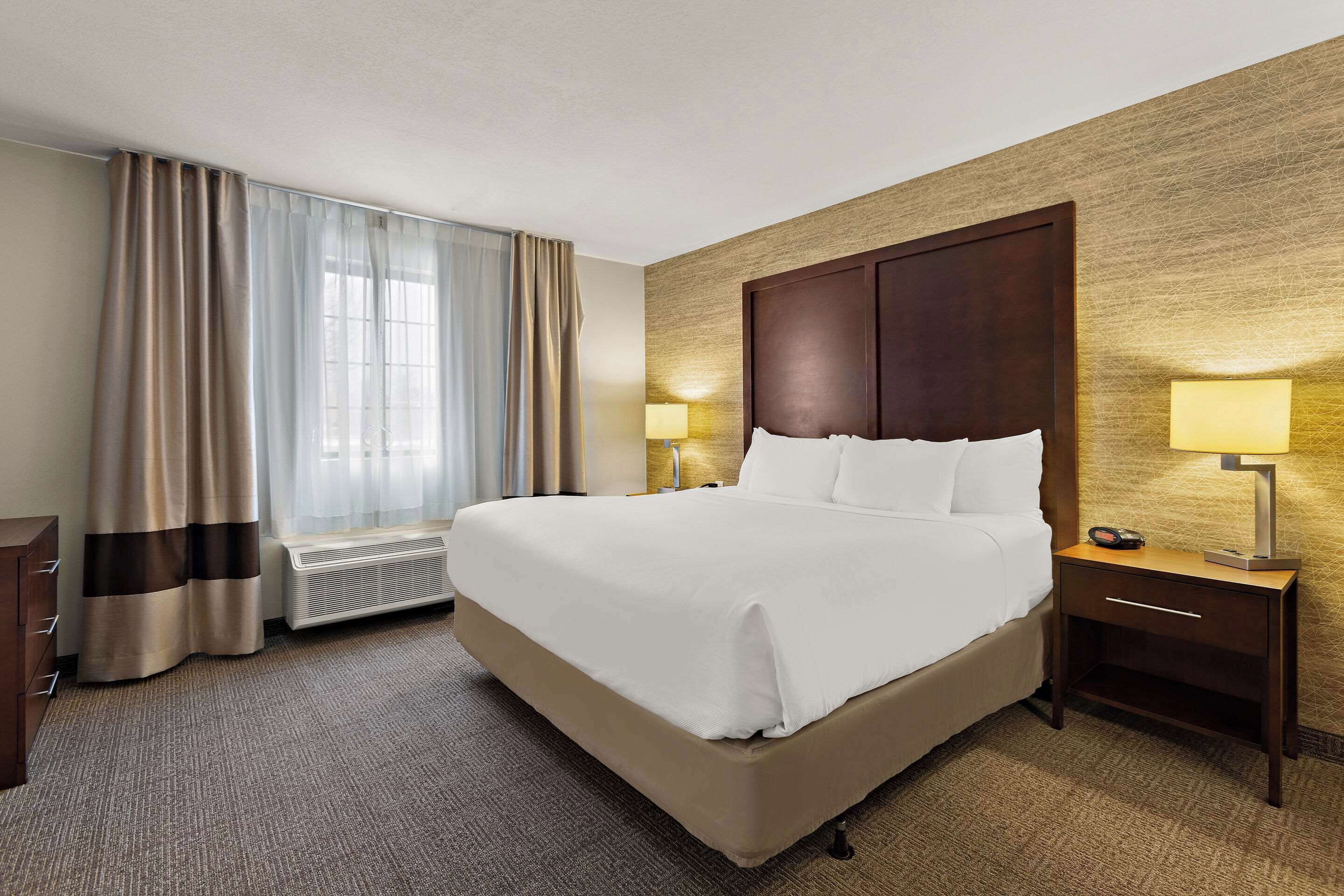 Una camera d'albergo con un letto grande, un comodino con una lampada, un termosifone e una finestra con tende.