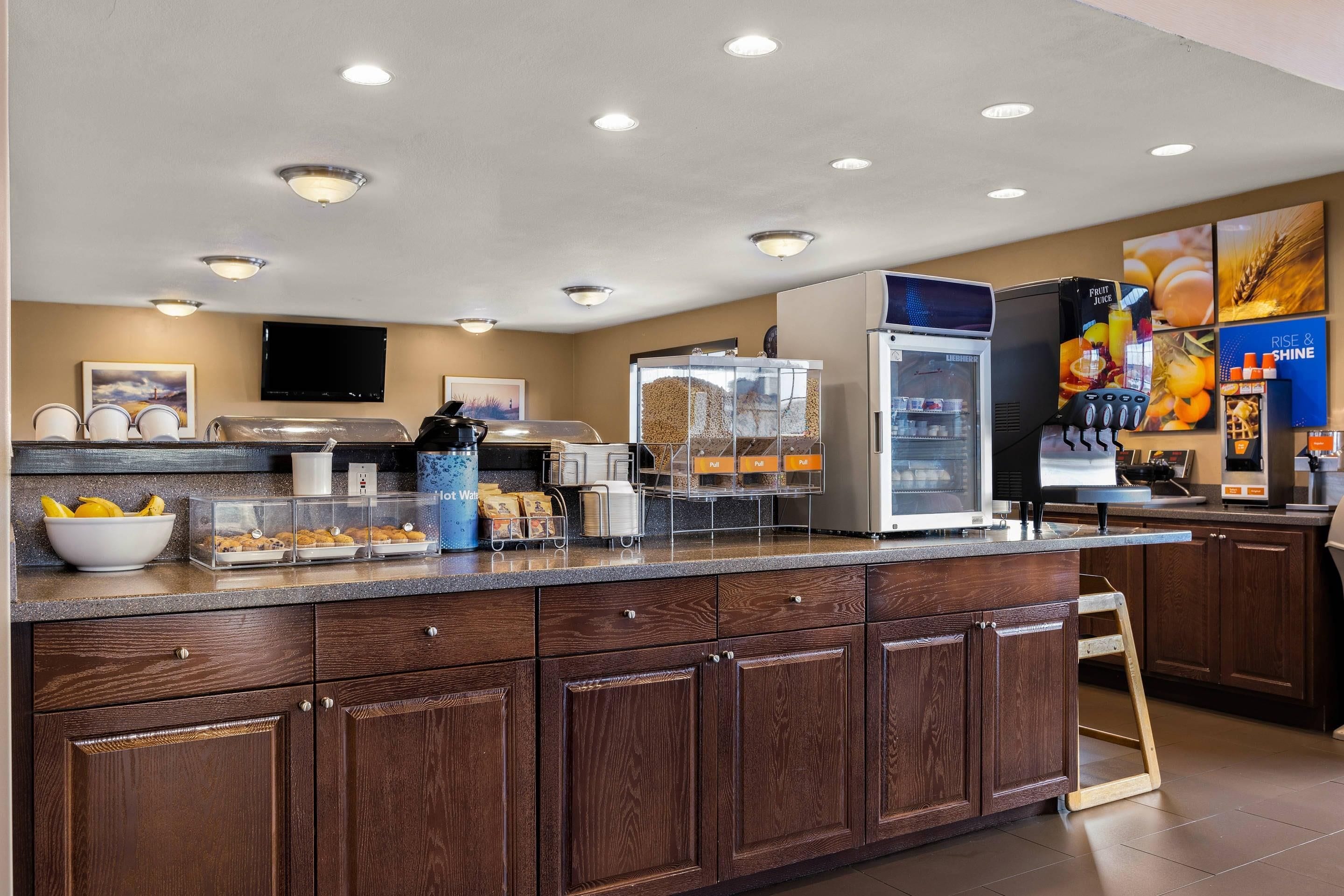 A self-service breakfast area with a coffee machine, refrigerated display, and a fruit juice dispenser.