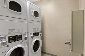Une buanderie équipée de deux machines à laver superposées et d’un sèche-linge, chacune dotée d’un écran numérique et de panneaux de commande.