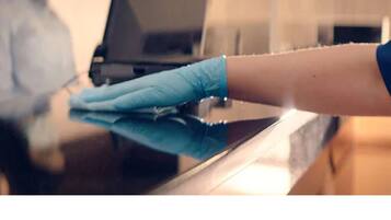 A hand wearing a blue glove cleaning a reflective surface, likely a countertop or table.