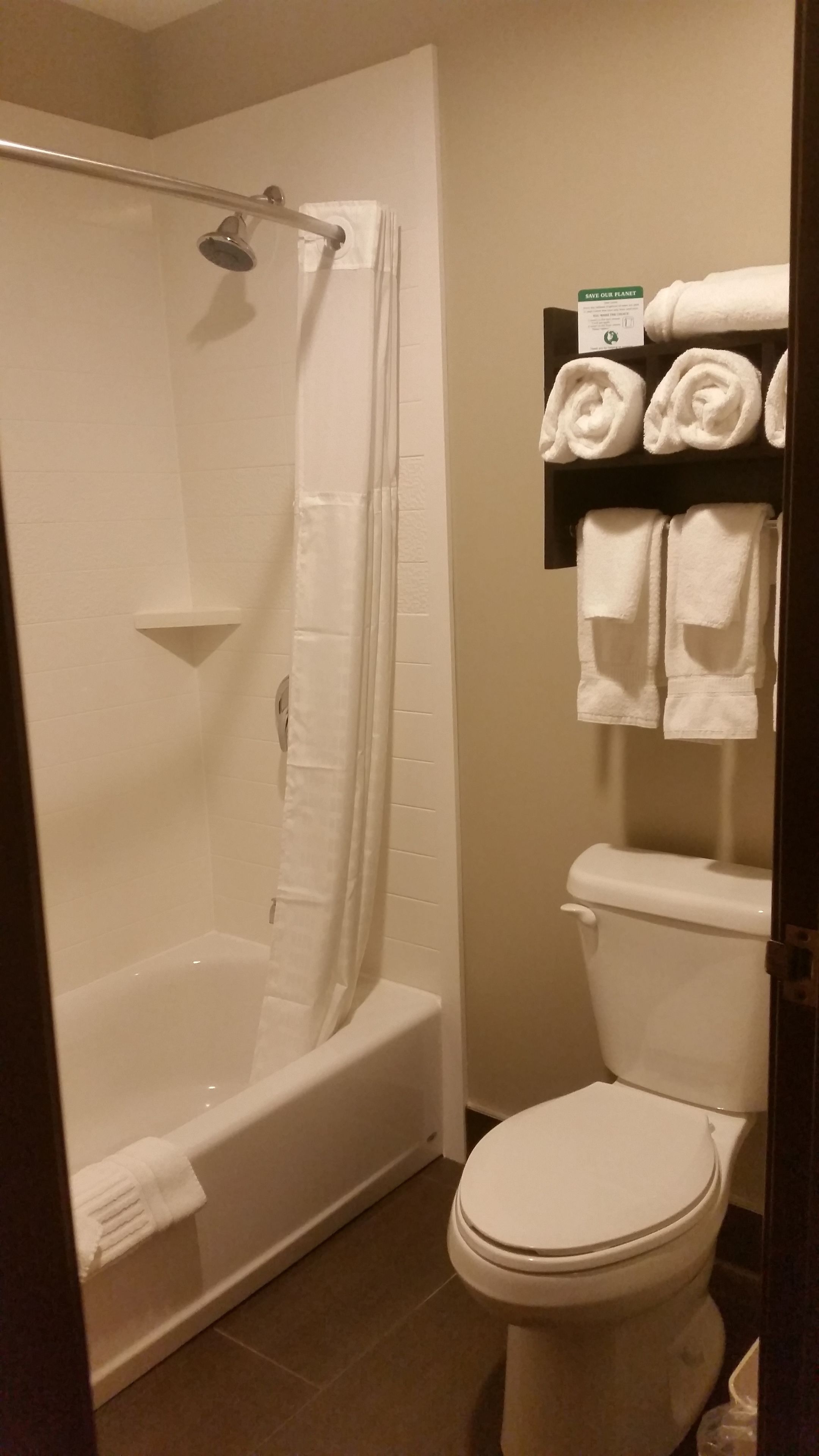 A bathroom with a bathtub, toilet, and a shelf with folded towels.