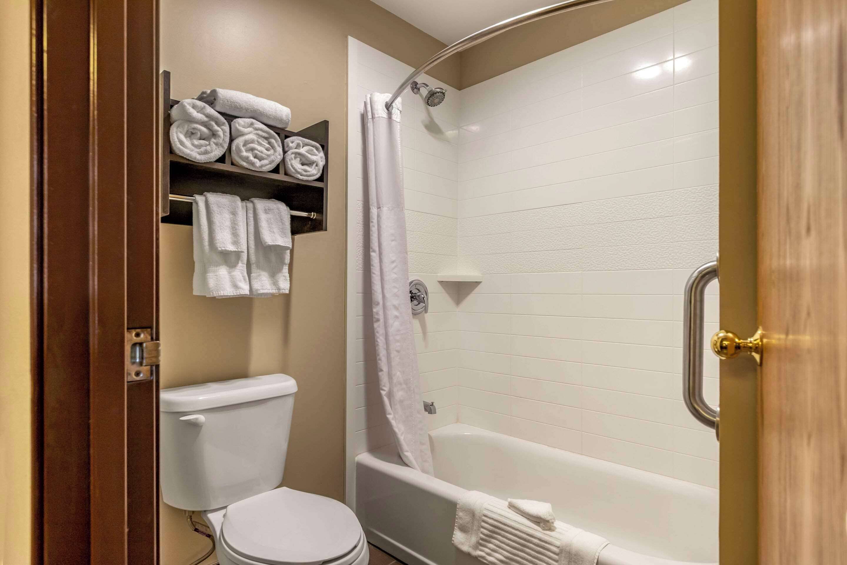 A bathroom with a toilet, a bathtub, and a shower curtain. There are towels on a shelf and a towel on the floor.