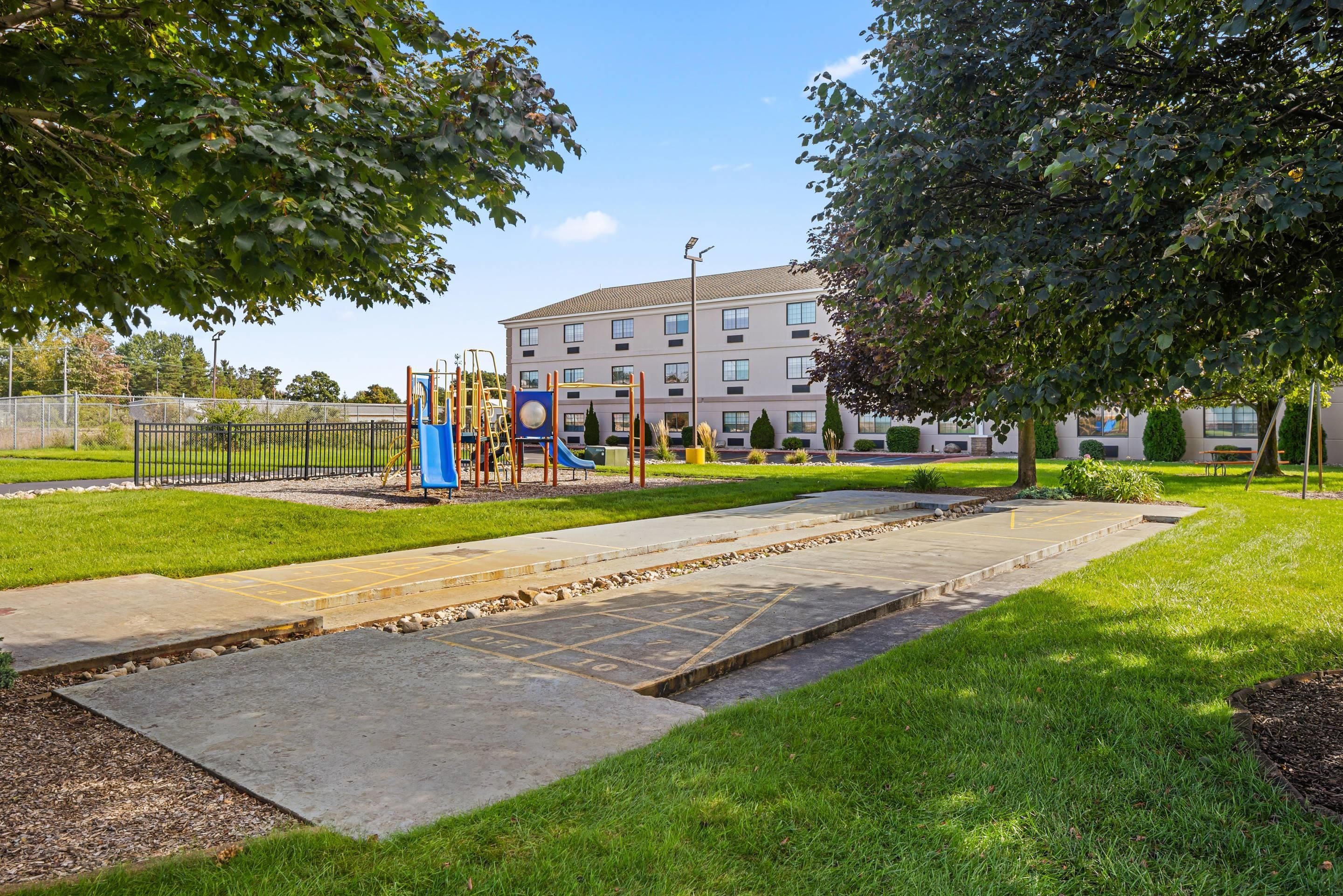 A playground with a slide and climbing structures, surrounded by a well-maintained lawn and a building in the background.