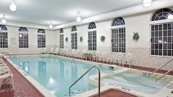 An indoor swimming pool with a hot tub, lounge chairs, and a poolside area.