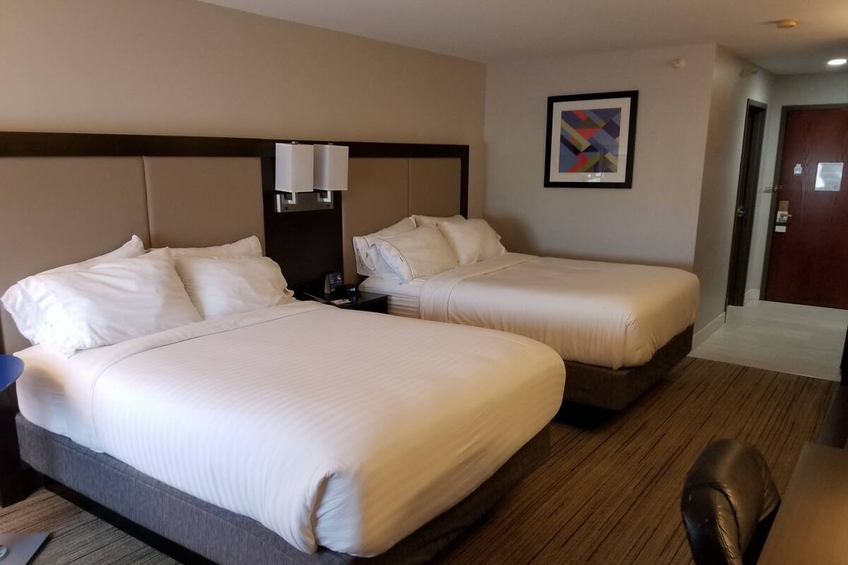 A hotel room with two beds, a desk, a chair, a nightstand, a lamp, and a framed picture on the wall.