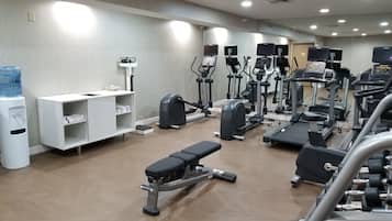 Un gimnasio con diferentes equipos de ejercicio, un dispensador de agua y un armario blanco con estantes.