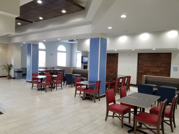 A spacious indoor area with multiple seating arrangements including tables and chairs, a television mounted on a wall, and a potted plant.