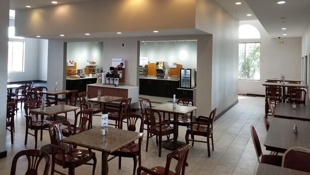 A spacious indoor dining area with multiple tables and chairs, a coffee station, and a counter with a menu display. - Holiday Inn Express Birch Run - Frankenmuth Area by IHG (Birch Run)