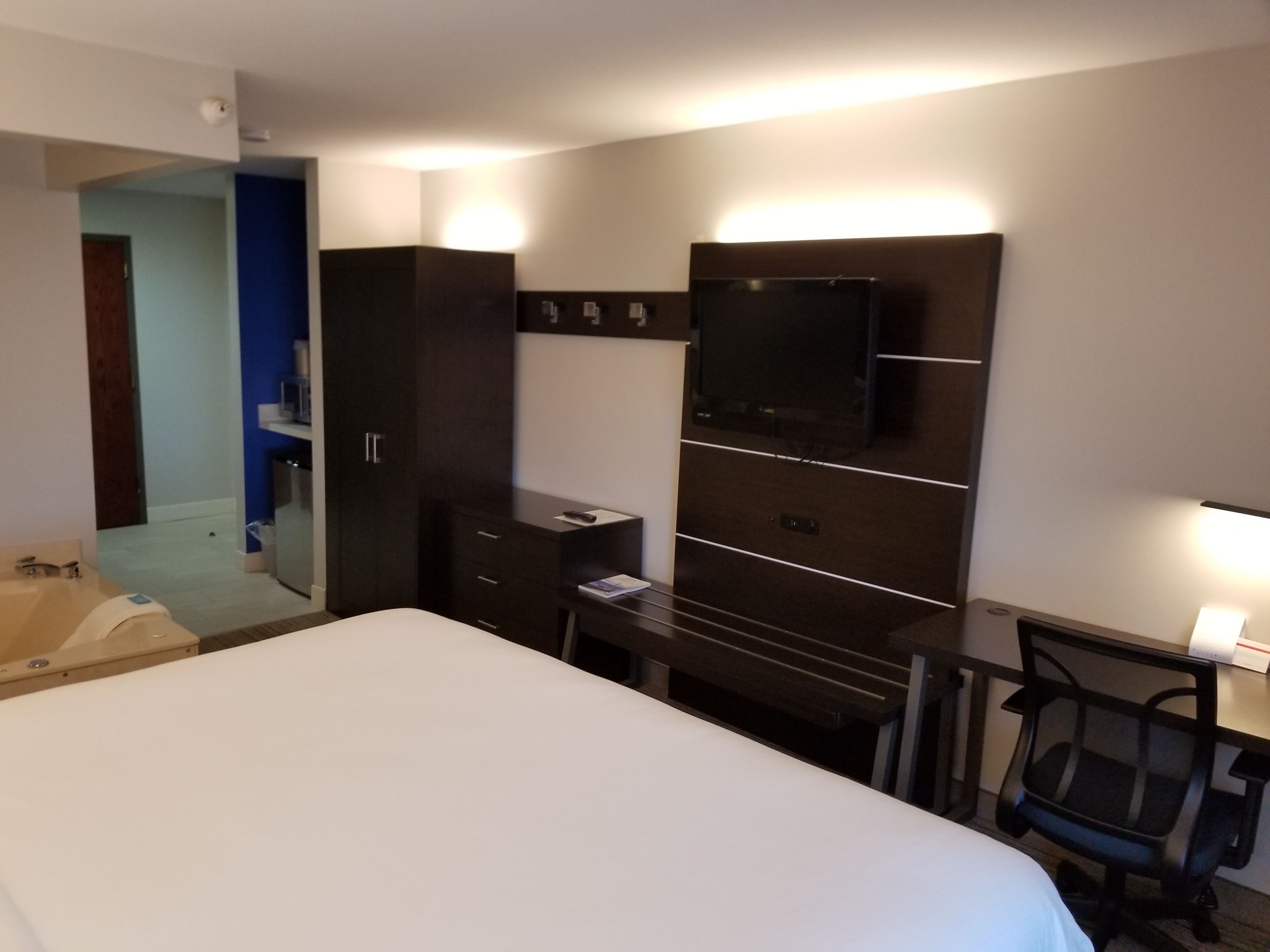A hotel room with a bed, a desk, a chair, a TV, and a wardrobe.