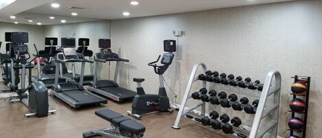 A gym with treadmills, elliptical machines, a bench press, and a rack of dumbbells.