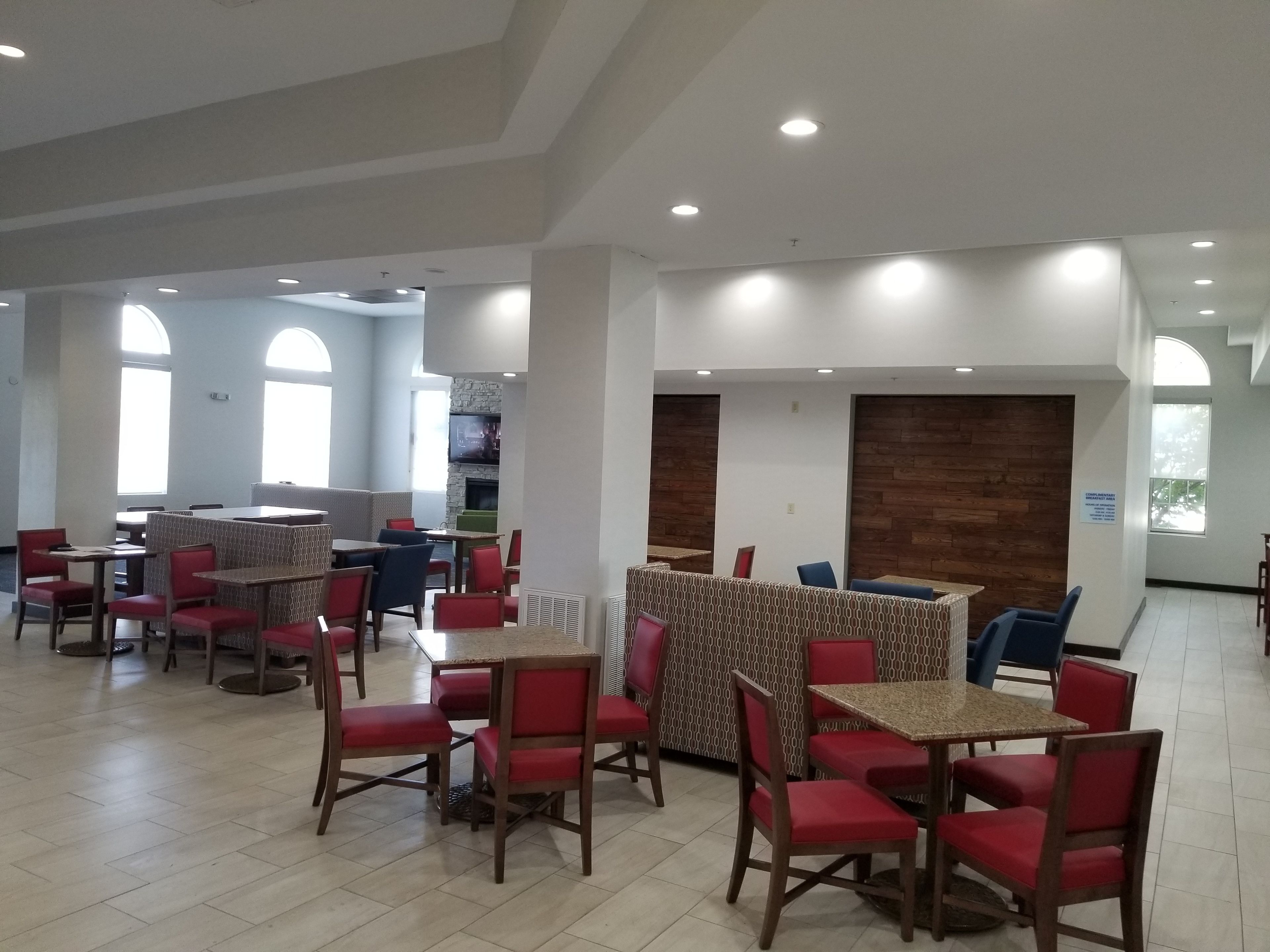 Un vaste espace de restauration intérieur, doté de nombreuses tables et chaises, de grandes fenêtres et d’un mur décoratif en pierre.