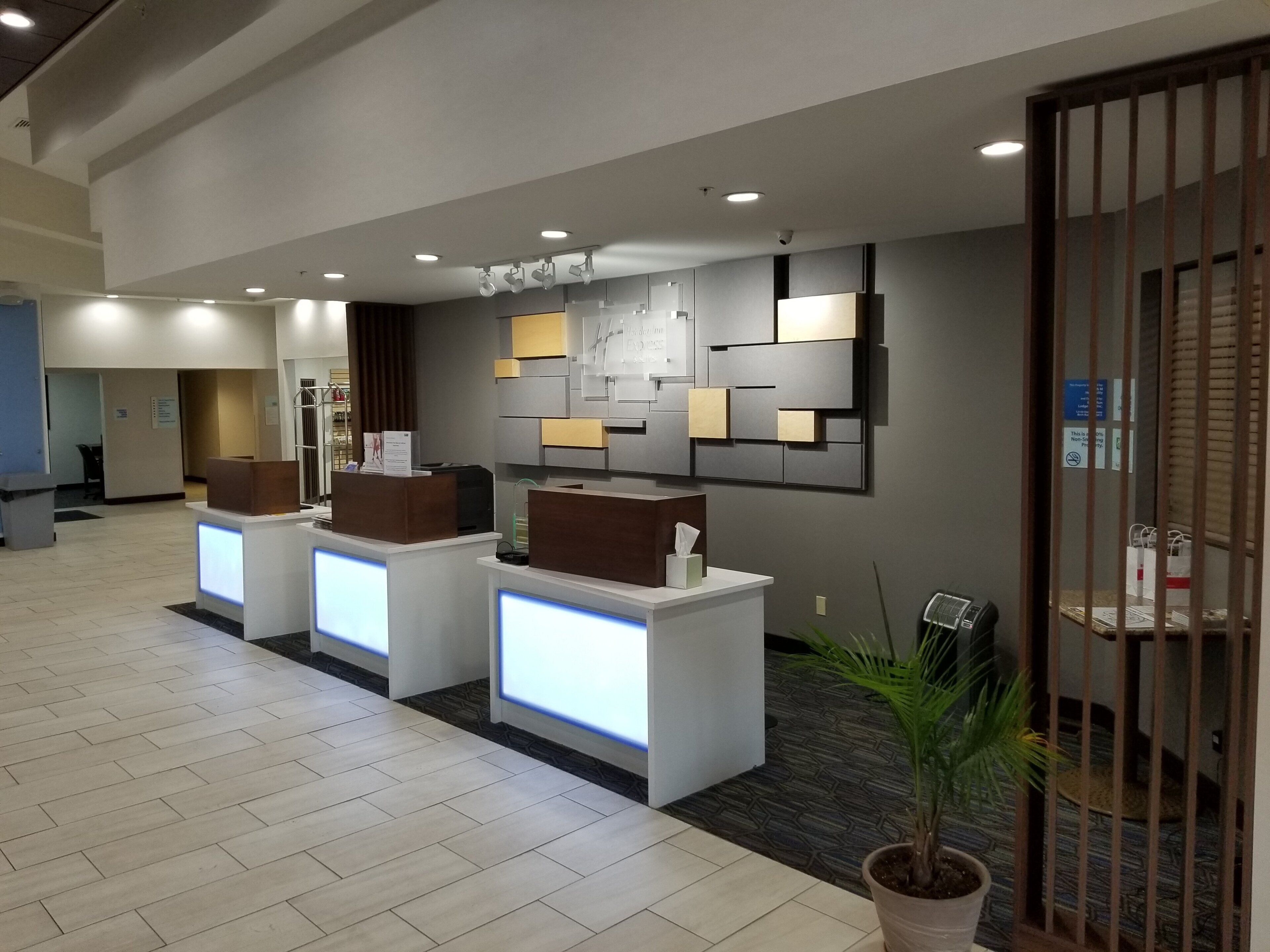 A reception area with a modern design, featuring a reception desk, a wall-mounted information board, and a potted plant.