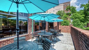 An outdoor patio area with brick walls, metal tables, and blue umbrellas.