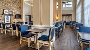 A restaurant with wooden flooring, blue upholstered chairs, and a brick wall with framed pictures.