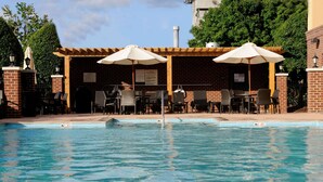 A pool area with lounge chairs and umbrellas, surrounded by brick walls and a pergola.
