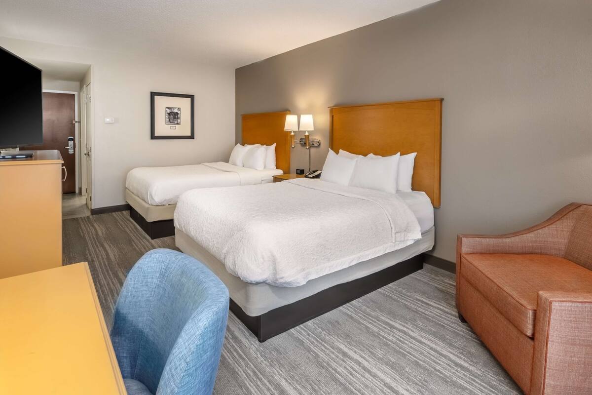 A hotel room with two beds, a desk, a chair, and a sofa.