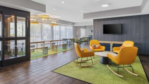 A modern lounge area with a large flat-screen TV, yellow rocking chairs, and a green carpet. - Spark by Hilton Bakersfield Central (Bakersfield)