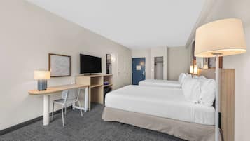 Habitación de hotel con cama, escritorio, silla, televisor y puerta.