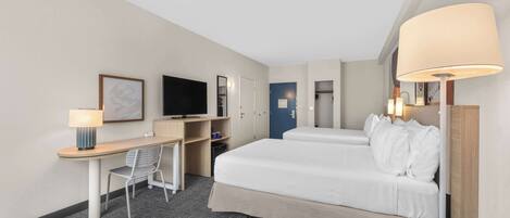 A hotel room with a bed, desk, chair, television, and a door.