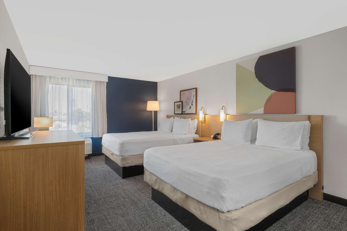 Habitación de hotel con dos camas, un escritorio, una lámpara, un teléfono y una ventana con cortinas.