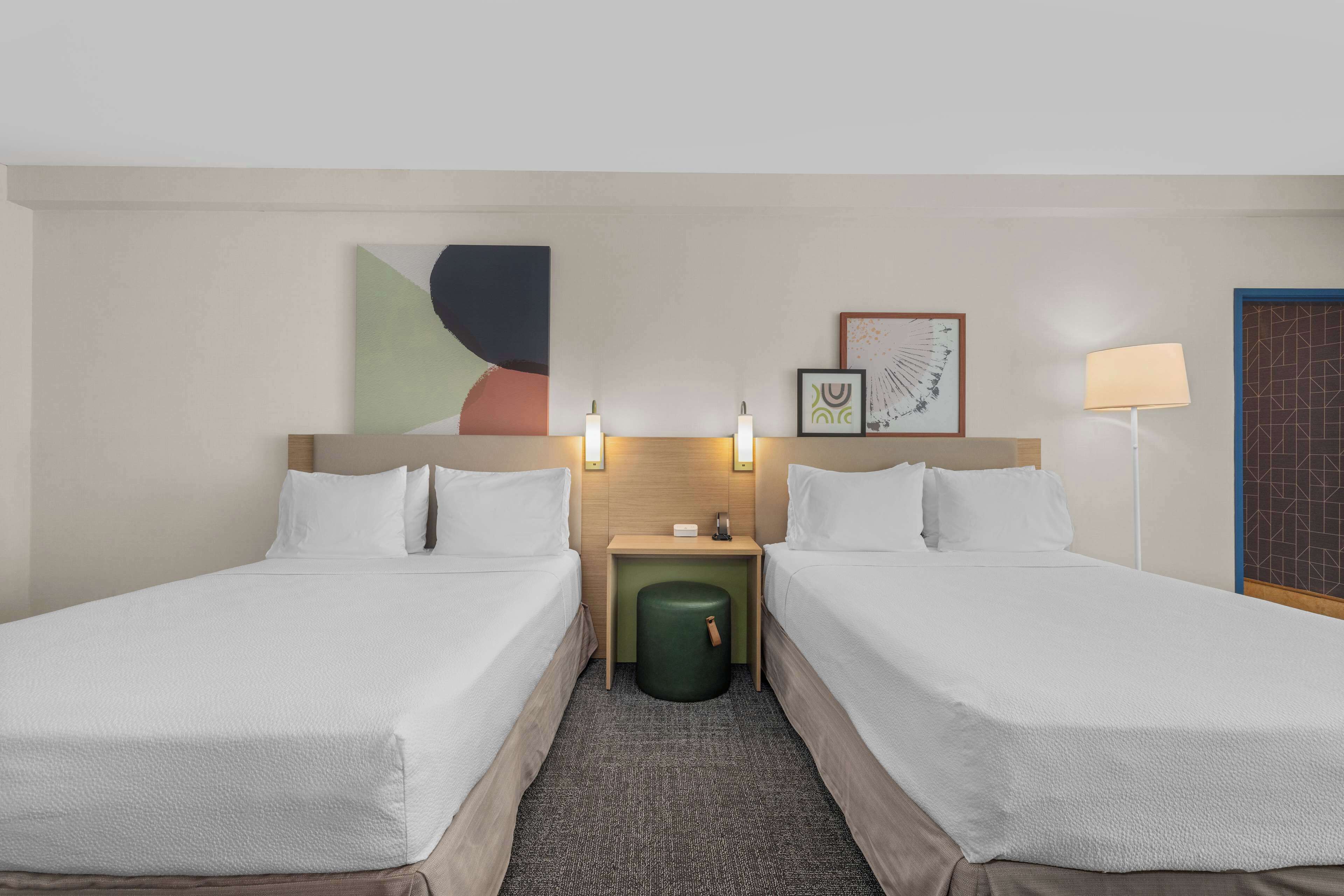 A hotel room with two single beds, a small bedside table with a lamp, and a wall-mounted artwork.