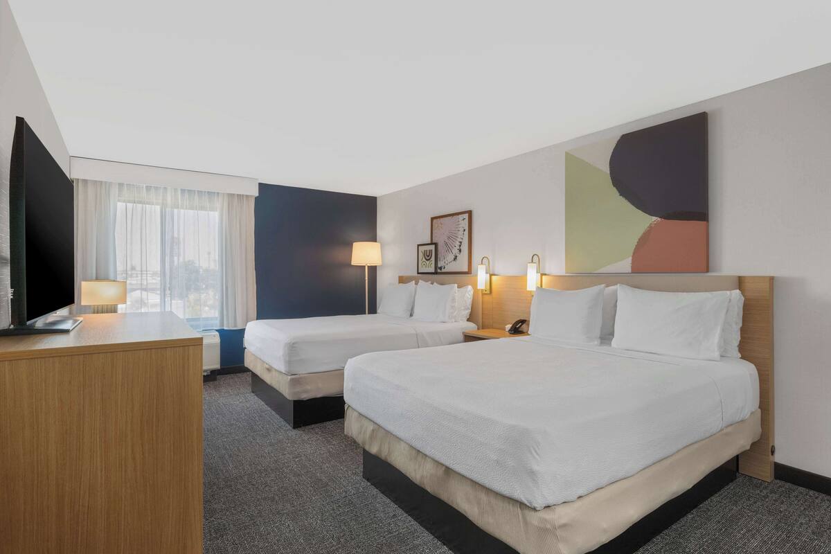 Una habitación de hotel con dos camas, un escritorio, una lámpara y un cuadro en la pared.