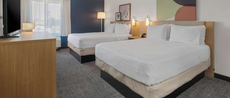A hotel room with two beds, a desk, a lamp, and a painting on the wall.