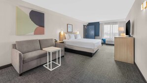 A hotel room with a bed, a sofa, a small table, a TV, and a painting on the wall. - Spark by Hilton Bakersfield Central (Bakersfield)