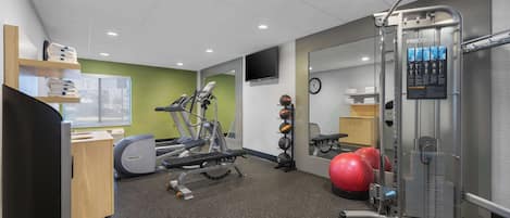 A gym with exercise equipment, a wall-mounted TV, and a red exercise ball.