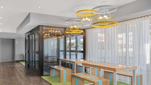 A modern conference room with glass walls, a wooden table with benches, and a green carpet. - Spark by Hilton Bakersfield Central (Bakersfield)