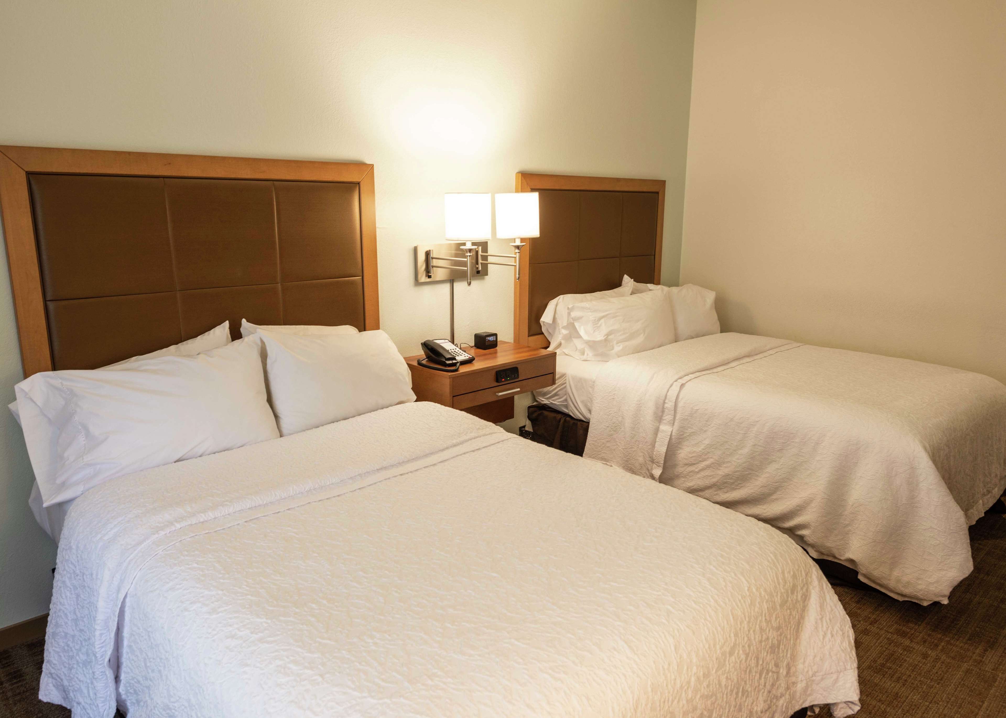 A hotel room with two beds, a nightstand with a lamp, and a telephone.