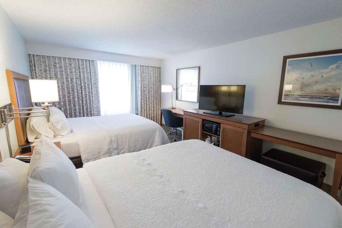 A hotel room with two beds, a desk, a television, and a painting on the wall.
